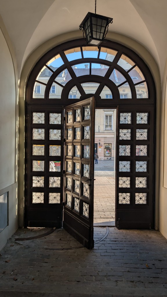 Otwarta drewniana brama z nadświetlem. Widok od sieni na Krakowskie Przedmieście